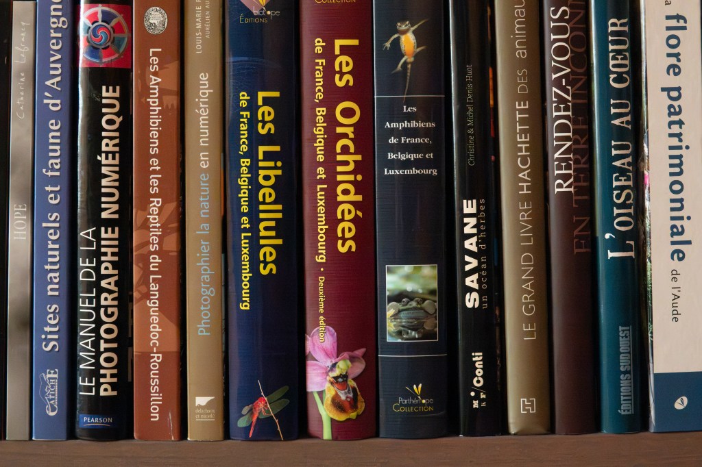Une étagère contenant une collection de livres sur la nature, la photographie, et la faune, incluant des titres sur les amphibiens et les libellules.